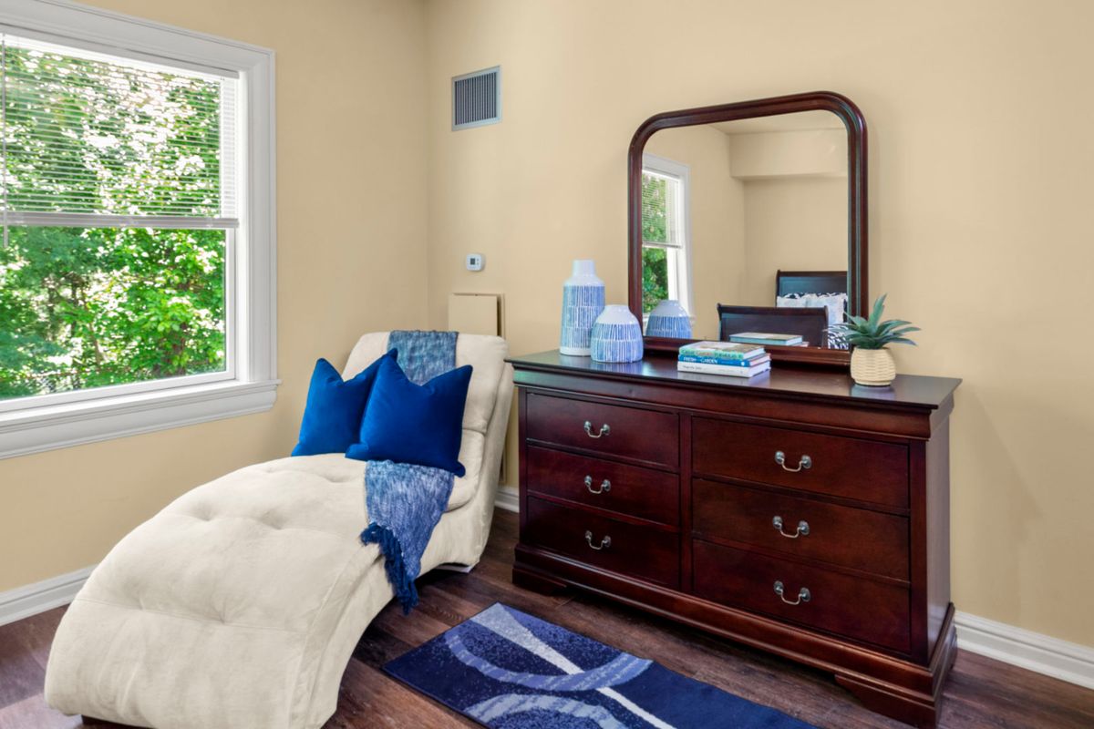 A cozy bedroom corner featuring a wooden dresser with a mirror and a comfortable chaise lounge adorned with blue pillows.