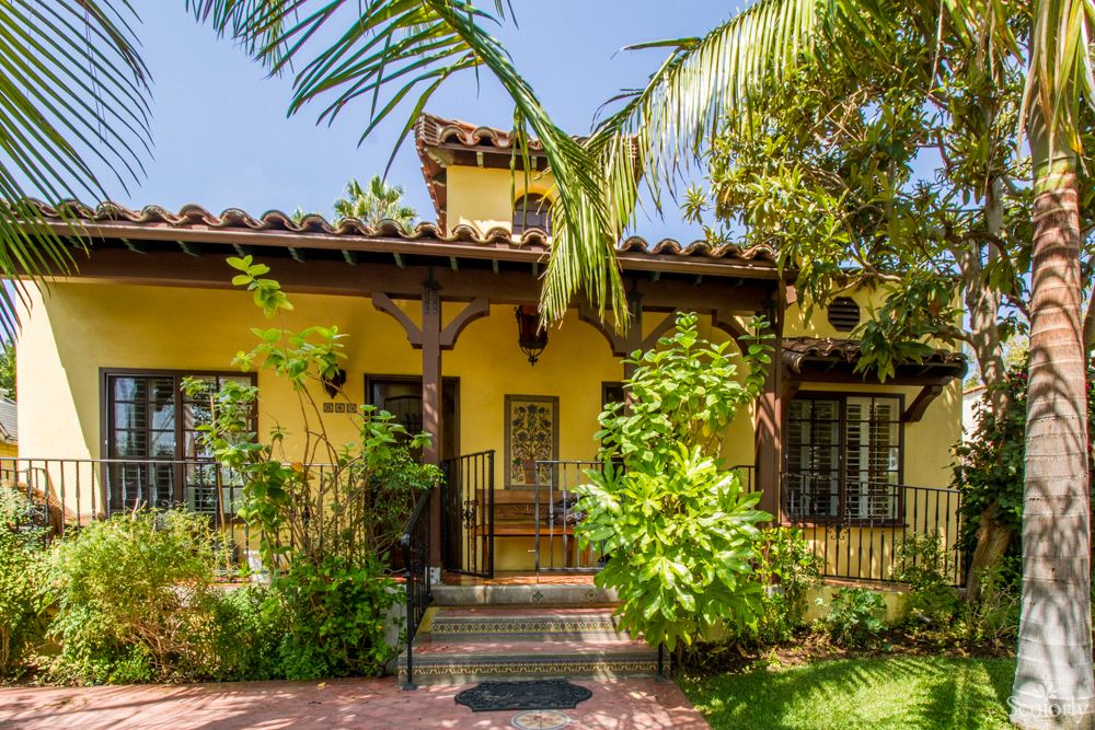 Charming Mediterranean-style house with a yellow exterior, surrounded by lush greenery and palm trees.