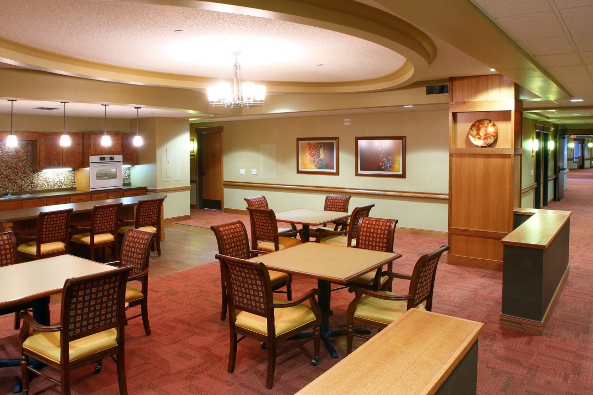 An interior view of a neatly arranged dining area with tables and chairs, featuring warm lighting and decor.