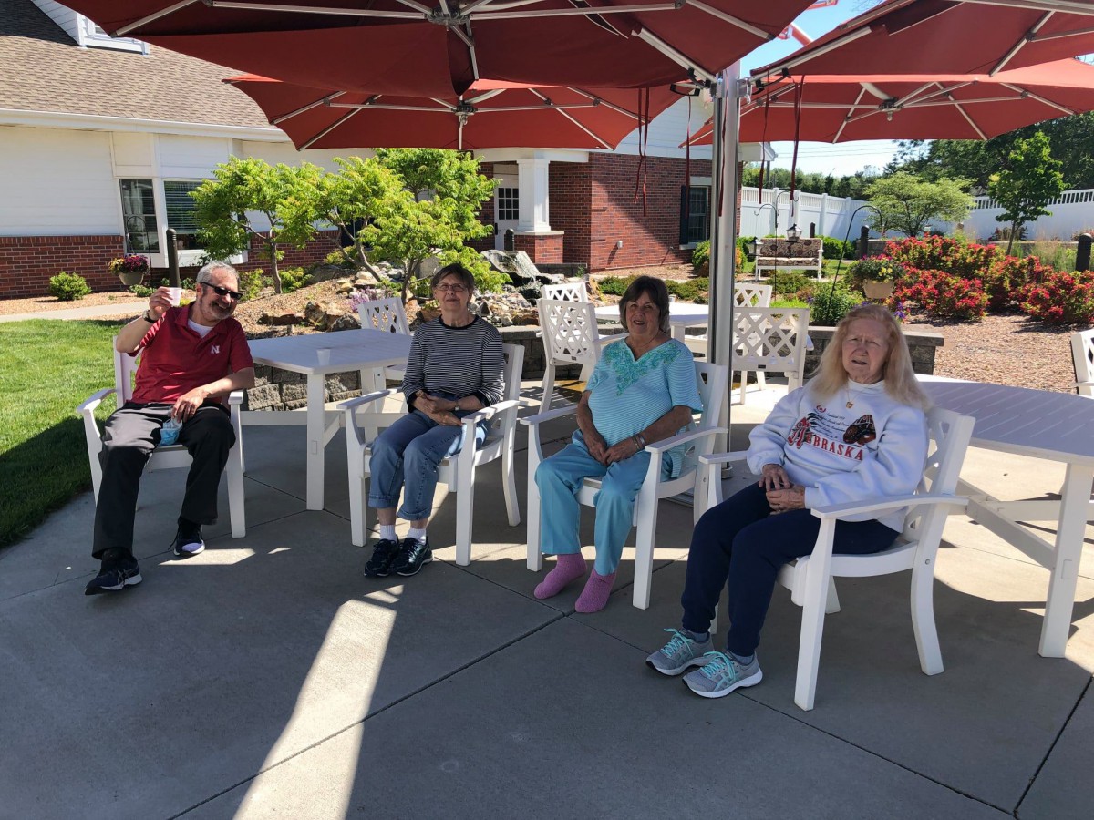 A group of people sitting outdoors under red umbrellas enjoying a sunny day.