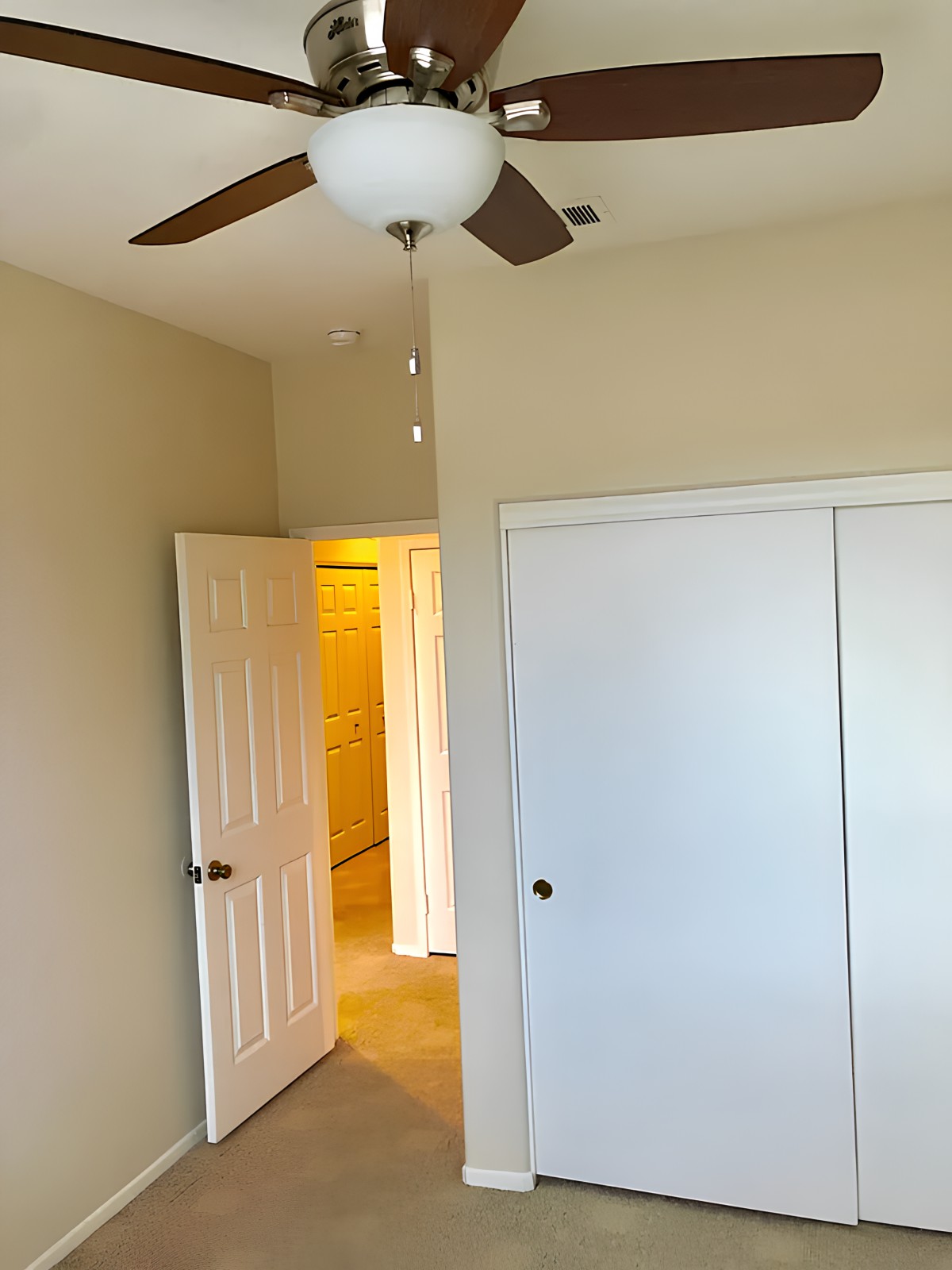 An empty bedroom with a ceiling fan and a closed closet door.