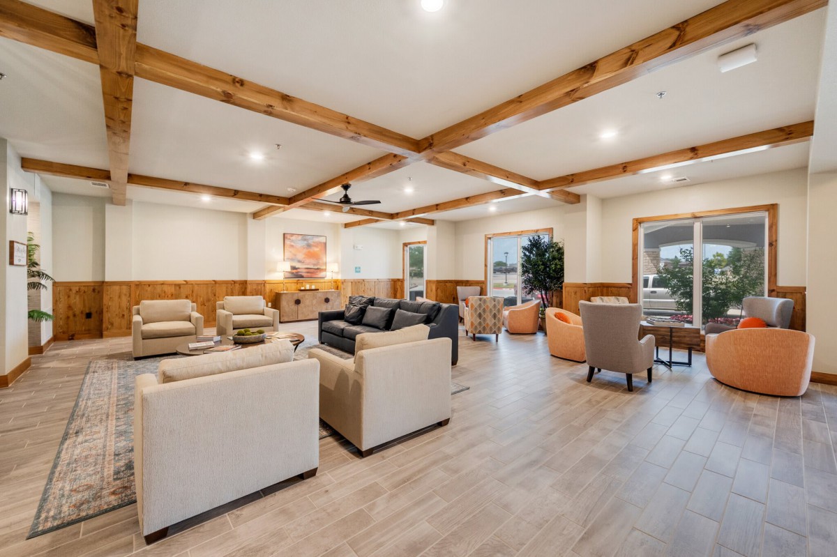 A spacious and modern living room featuring wooden ceiling beams, neutral-toned furniture, and ample lighting.