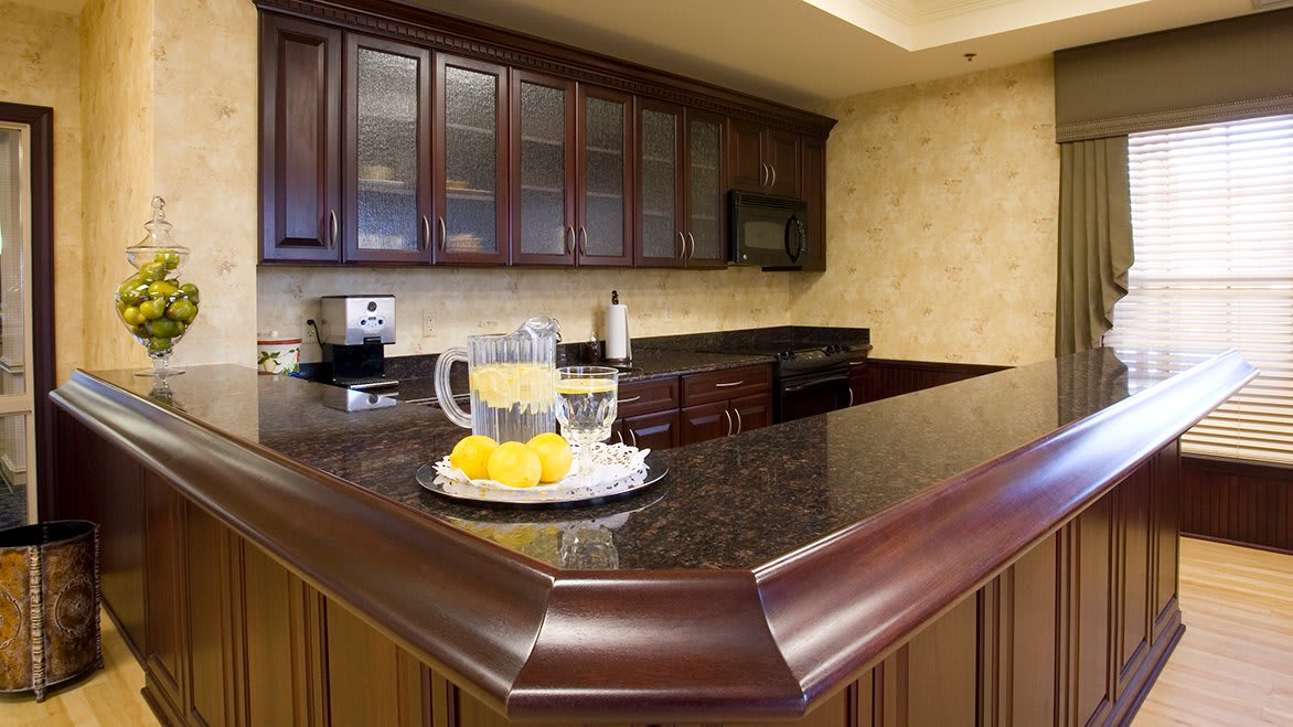A cozy kitchen with dark wood cabinets and a granite countertop, featuring a pitcher of lemonade and fresh lemons.