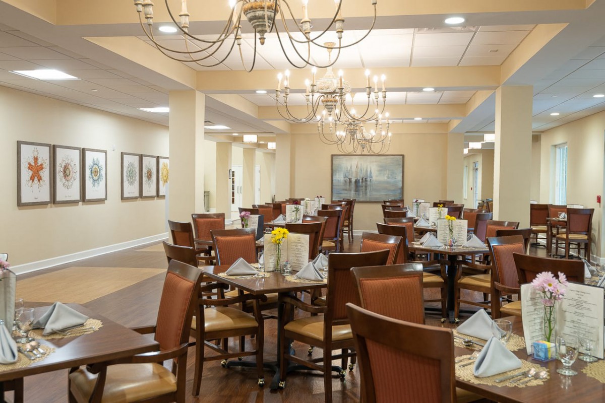 An elegant dining room with neatly set tables and chandeliers overhead.