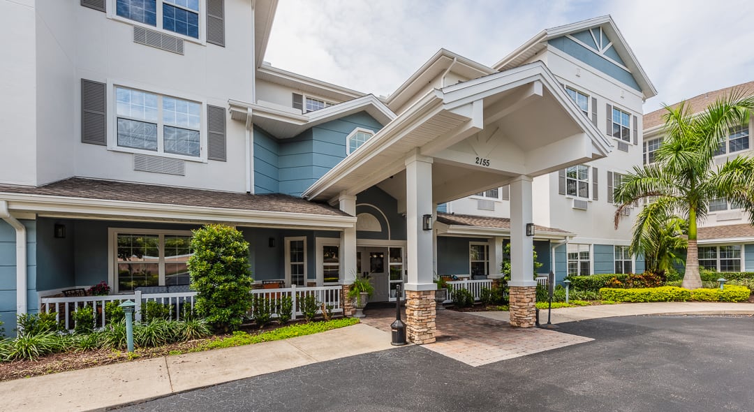 The image shows the entrance of a residential building with a porch and landscaped surroundings.