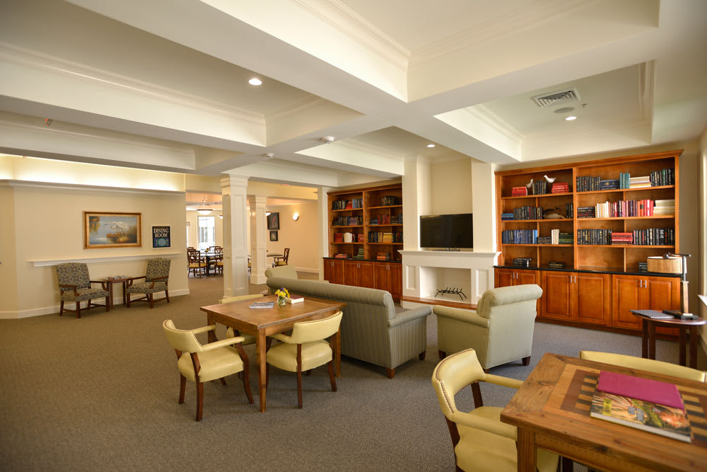 A spacious and well-lit living room with multiple seating areas, bookshelves, and a fireplace.