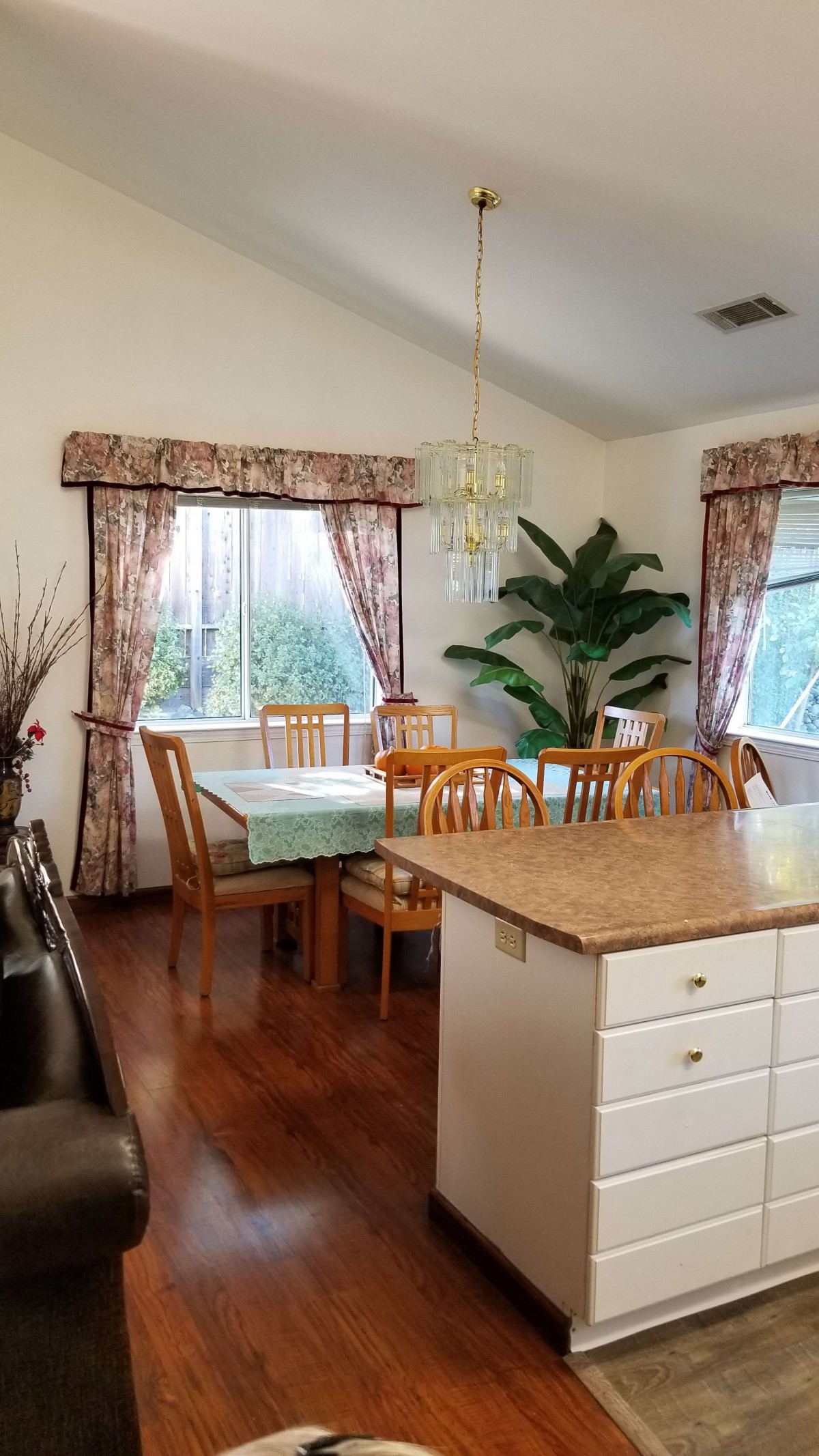 A cozy dining area with a wooden table and chairs, complemented by green plants and natural light through large windows.