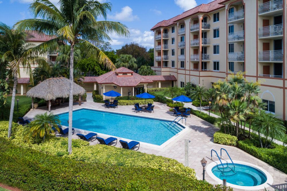 A tropical hotel setting with a pool surrounded by palm trees and outdoor seating.