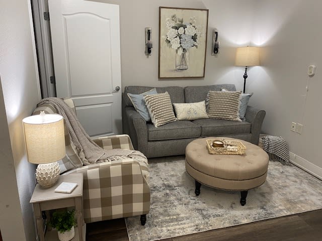 A cozy living room with a gray sofa, plaid armchair, and a round beige coffee table.