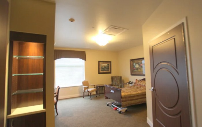 A well-lit room with a bed, chair, and window featuring decorative artwork.