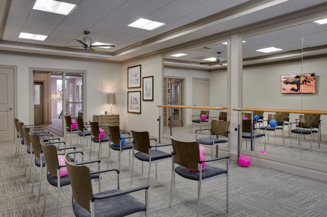 A spacious room with chairs arranged in rows, featuring yoga exercise balls and mirrors along the walls.