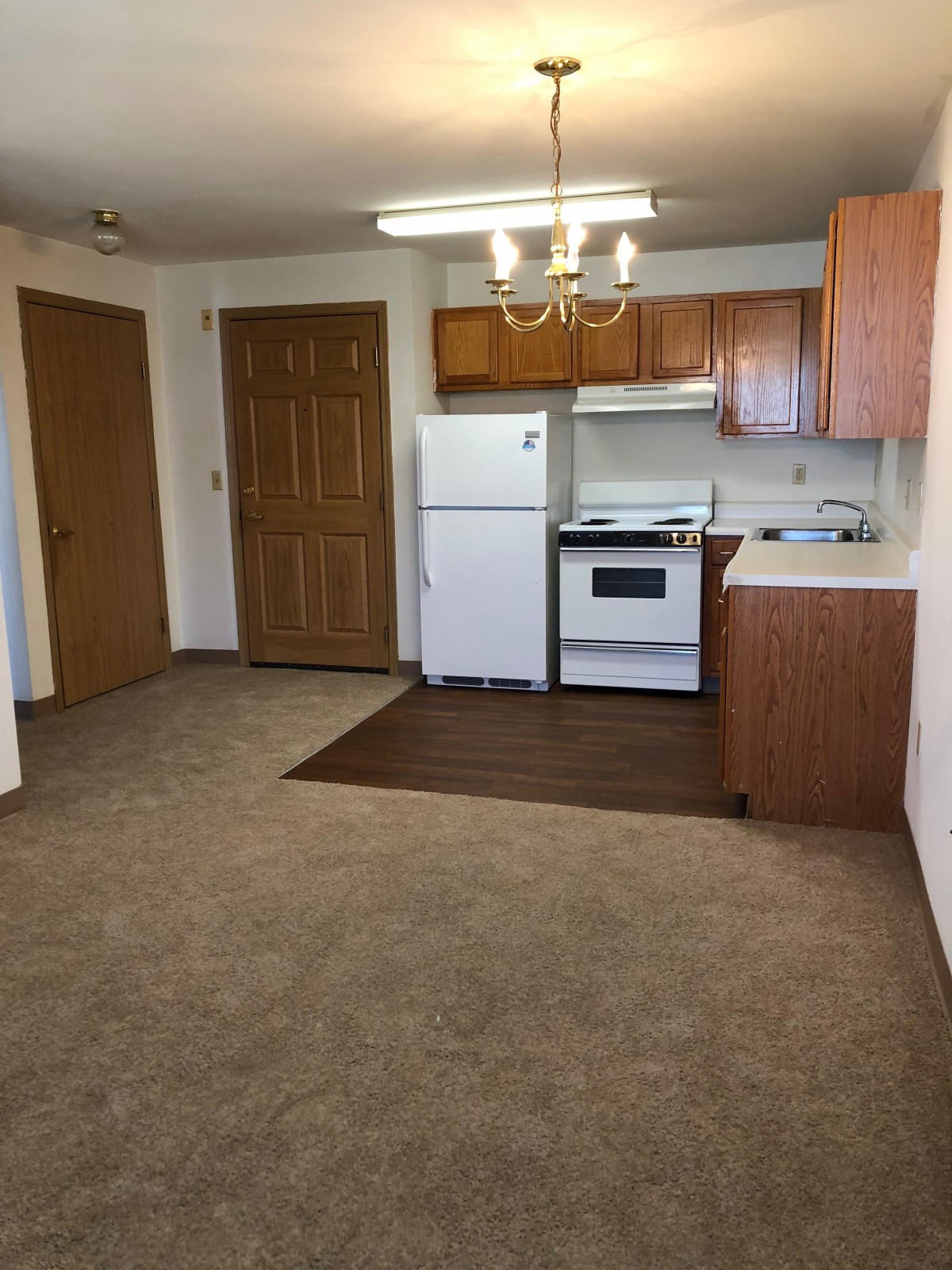 An empty apartment kitchen with wooden cabinets, a refrigerator, and an oven.