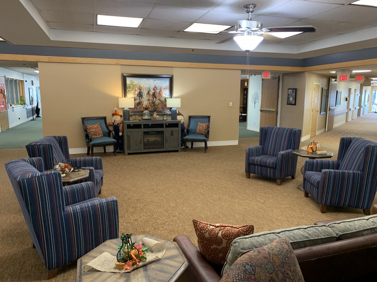 A cozy living room with chairs and a sofa arranged around a central table, featuring warm lighting and decorative elements.