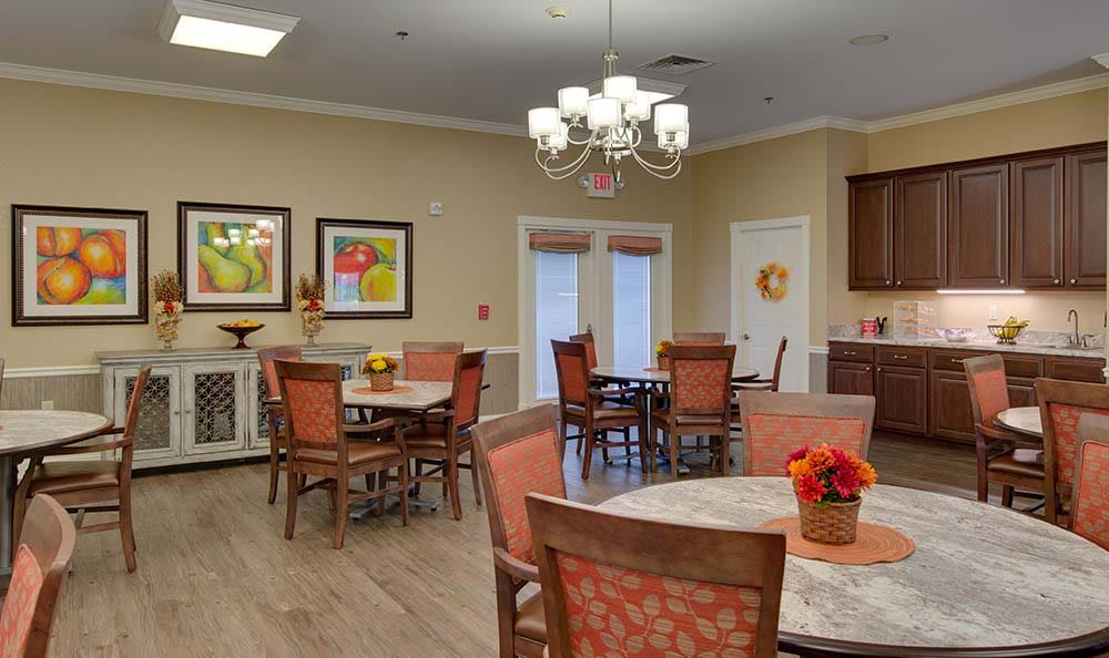 A cozy dining room with several tables and chairs, decorated with floral arrangements and paintings on the walls.