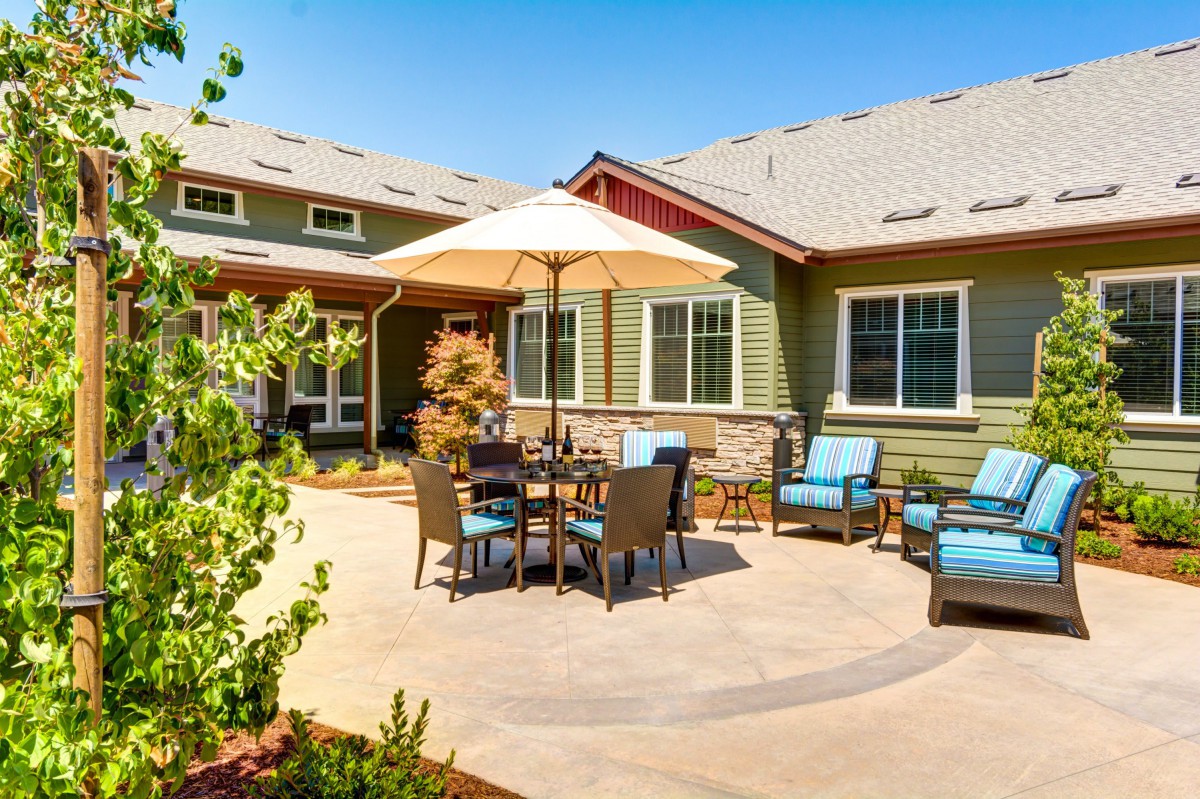 A sunny backyard patio with outdoor furniture and an umbrella.