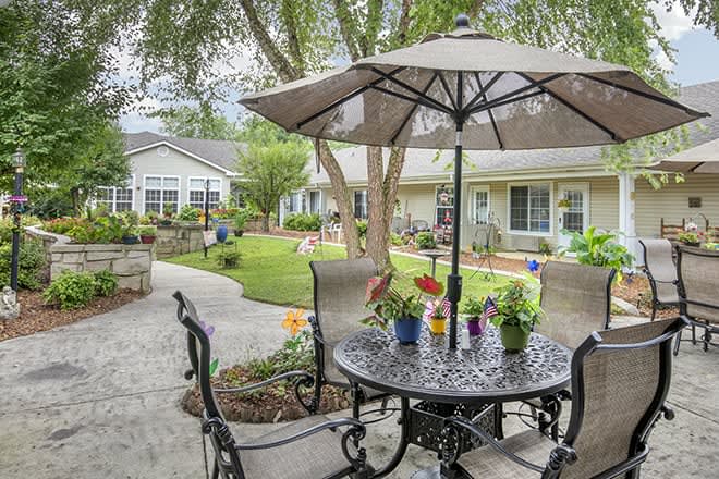 A cozy outdoor patio area with a table, chairs, and an umbrella, surrounded by a well-maintained garden.