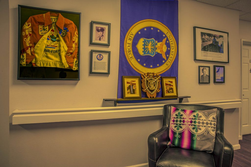 An office space featuring a flag, framed memorabilia, and a couch with colorful cushions.
