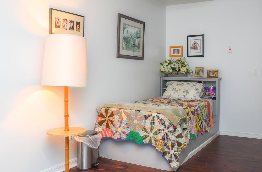 A cozy bedroom with a single bed adorned with a colorful quilt, surrounded by artwork and soft lighting.