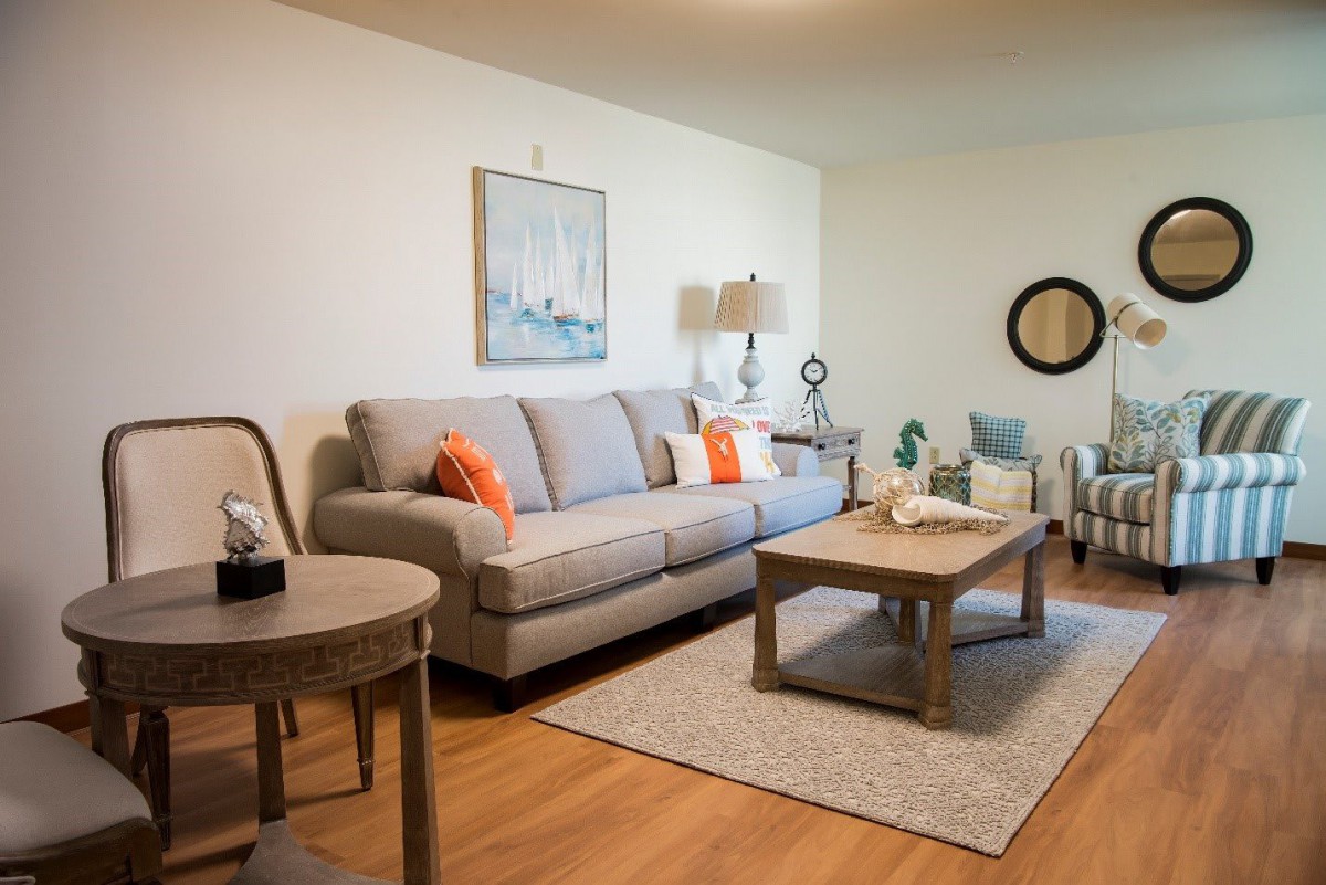 A cozy living room with a gray sofa, decorated with orange cushions, a wooden coffee table, and various decorative items.