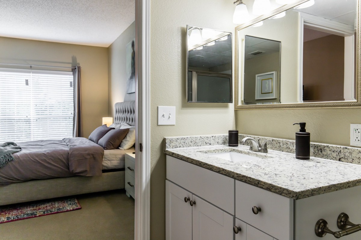 A bathroom with a granite countertop and a view into an adjacent bedroom.