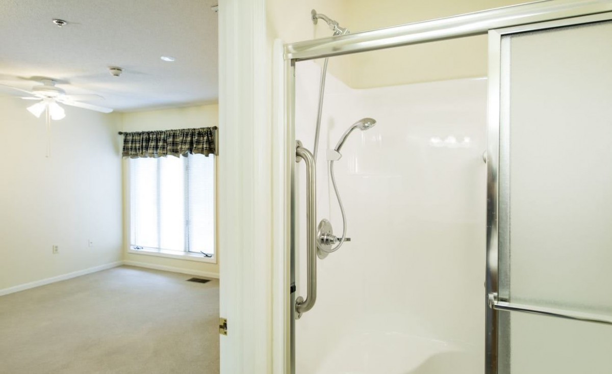 Modern bathroom with a glass shower enclosure and adjacent room view.