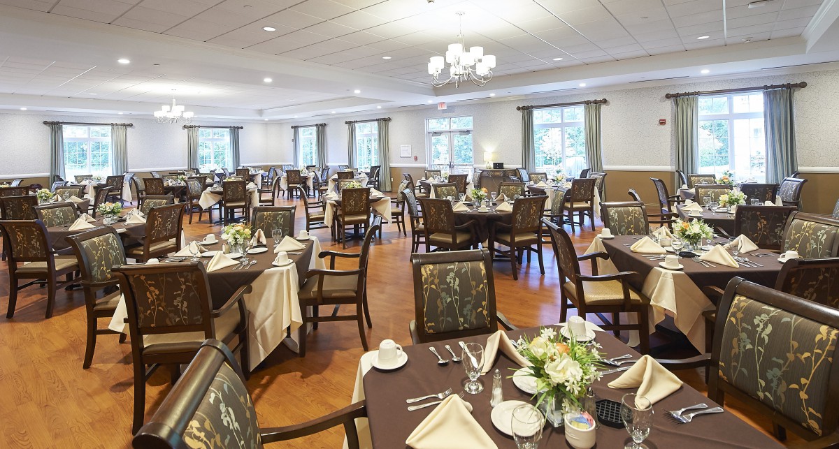 A spacious and elegantly set dining room with multiple tables and chairs, adorned with chandeliers.