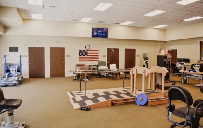 Interior of a physical therapy facility with various exercise equipment and an American flag on the wall.