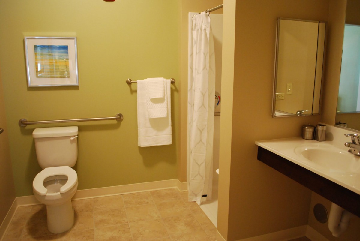 A clean and modern bathroom featuring a toilet, shower, and sink with a mirror and towel rack.