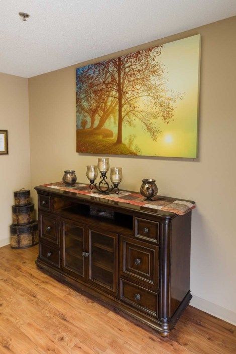 A cozy living room with a wooden sideboard adorned with decorative items and a large painting of a tree hanging above it.