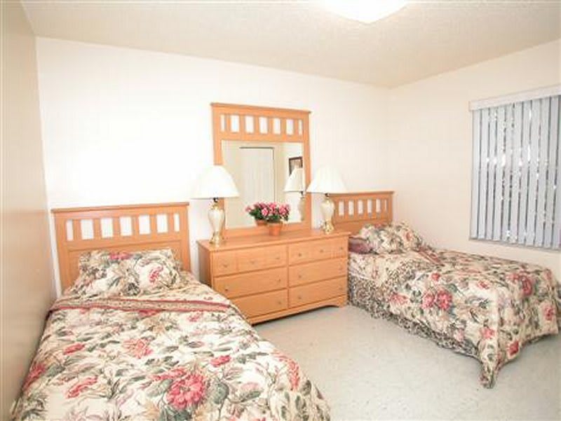 A cozy bedroom with twin beds and floral bedding features a wooden dresser with a mirror and decorative lamps.