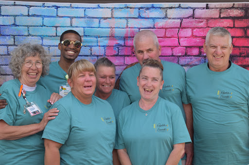 A cheerful group of friends posing together against a vibrant blue and pink wall.