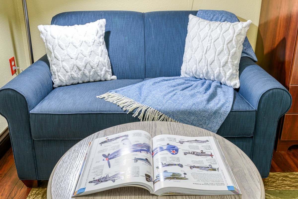 A cozy living room setup with a blue sofa, decorative pillows, a blanket, and an open magazine on the coffee table.