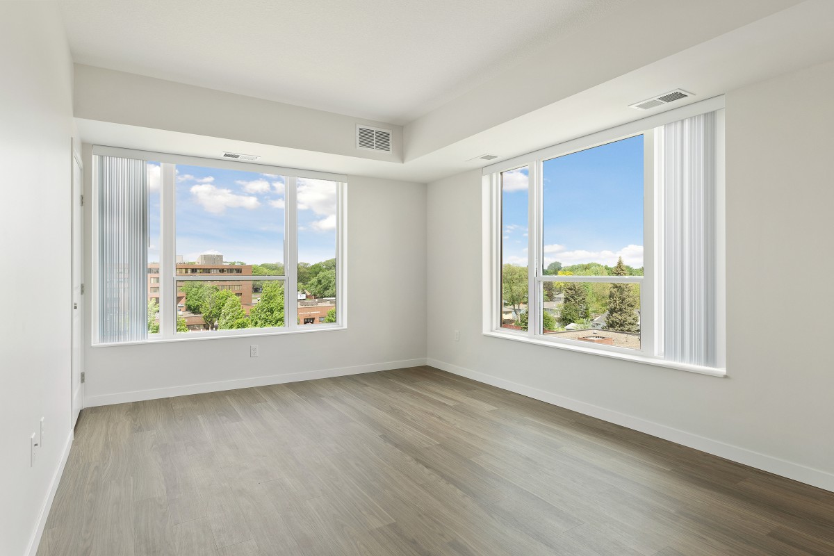 A bright, empty room with large windows and hardwood flooring.