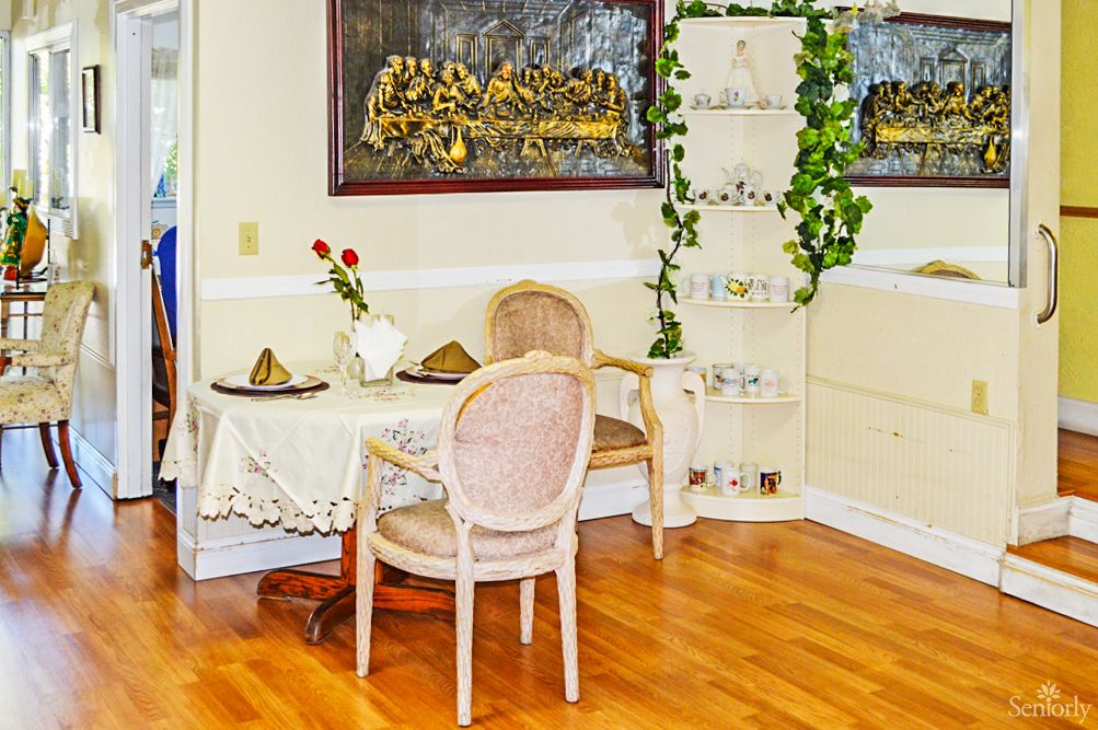 A cozy dining area with a small table, two chairs, decorative plants, and artwork on the walls.
