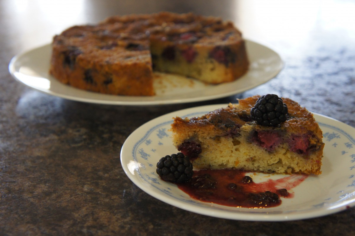 A slice of blackberry cake served on a plate, with the rest of the cake in the background.