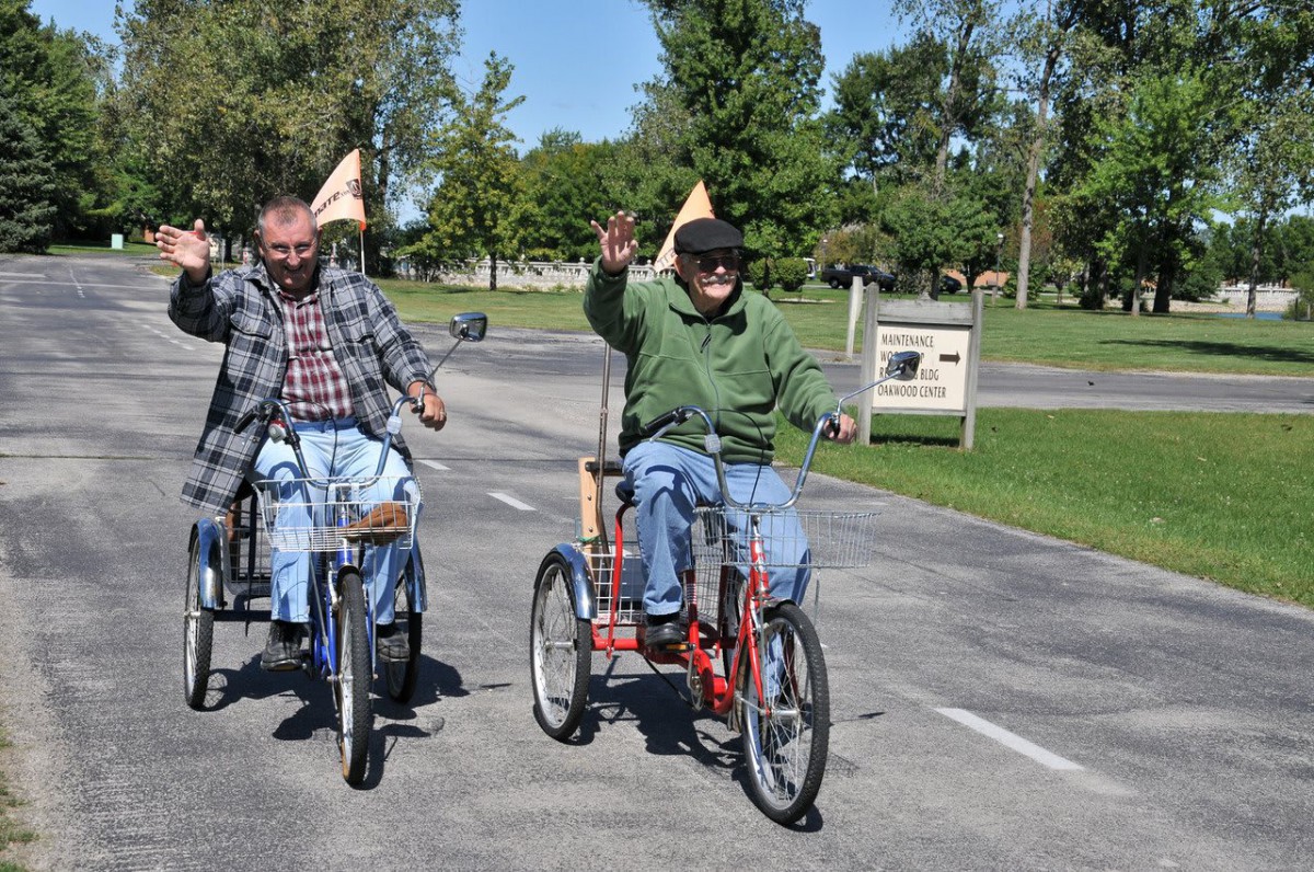 Two men riding tricycles on a sunny day, enjoying the outdoors.