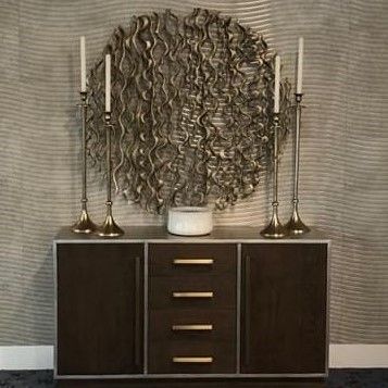 A stylish sideboard adorned with tall candlesticks and a decorative vase, set against textured wall art.