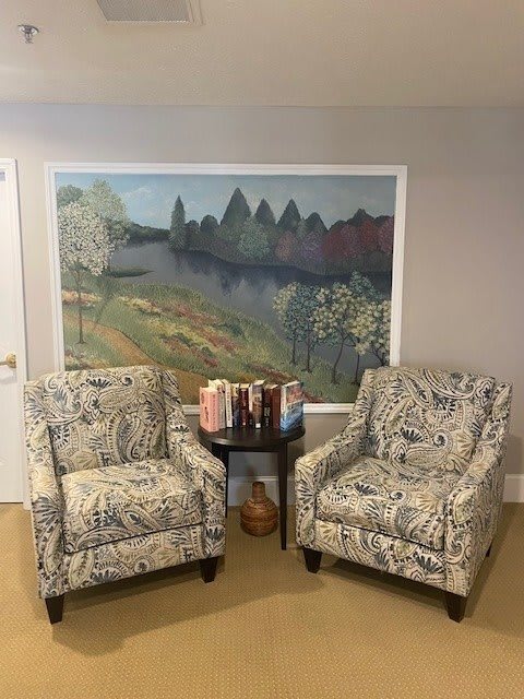 A cozy living room setup with two patterned armchairs flanking a small side table, set against a large landscape painting.