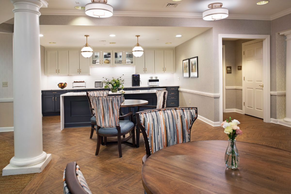 A modern dining area with a kitchen in the background, featuring stylish furniture and lighting.