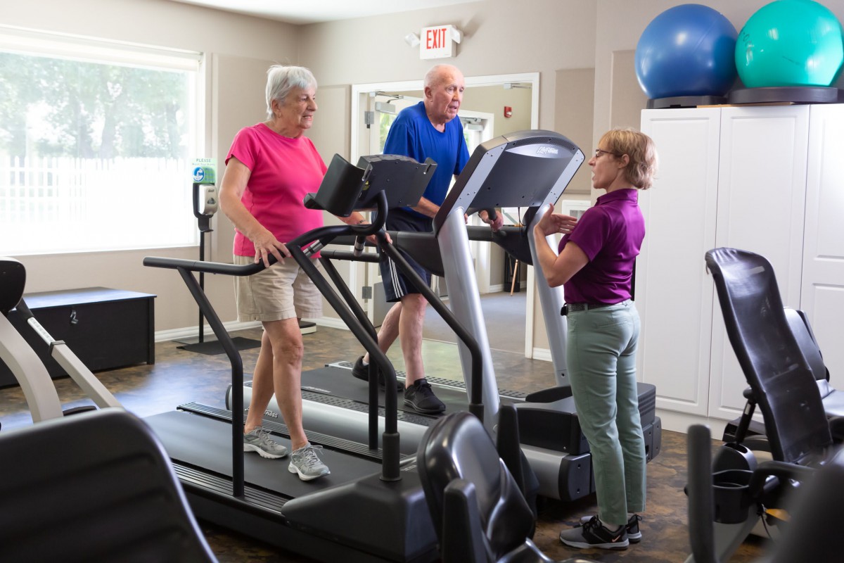 Seniors exercising on treadmills with a trainer in a fitness center.