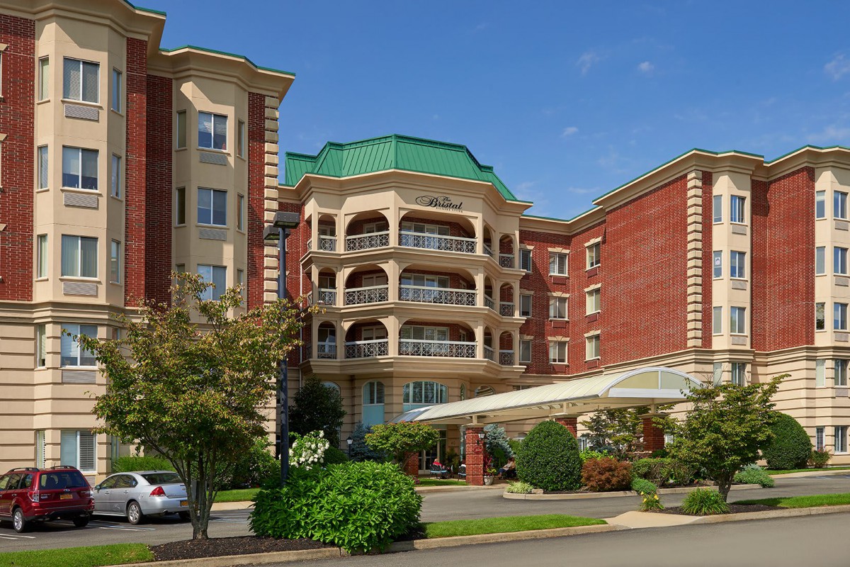 A grand hotel building with a green roof, surrounded by trees and a well-maintained garden.