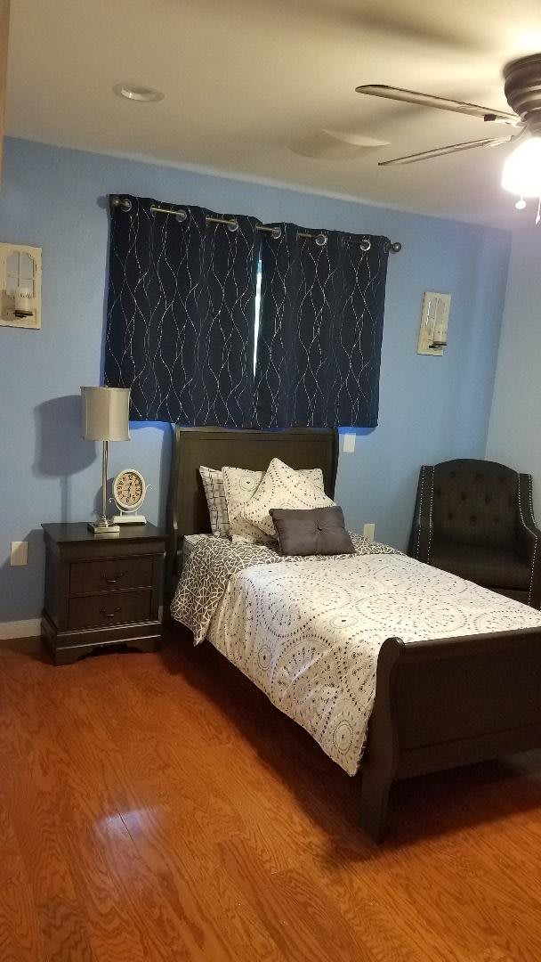 A cozy bedroom with blue walls, featuring a single bed, nightstand, and armchair.