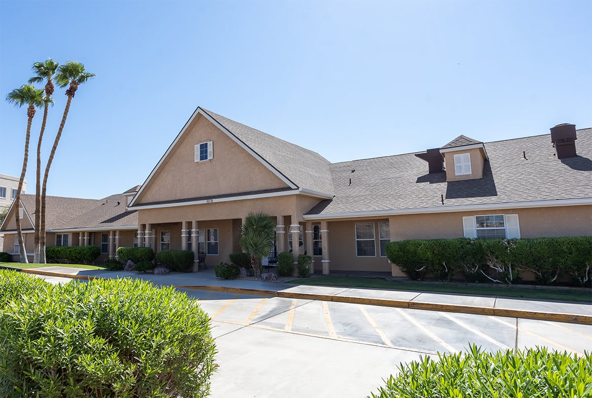 A suburban residential building with a sloped roof and front yard greenery under a clear blue sky.