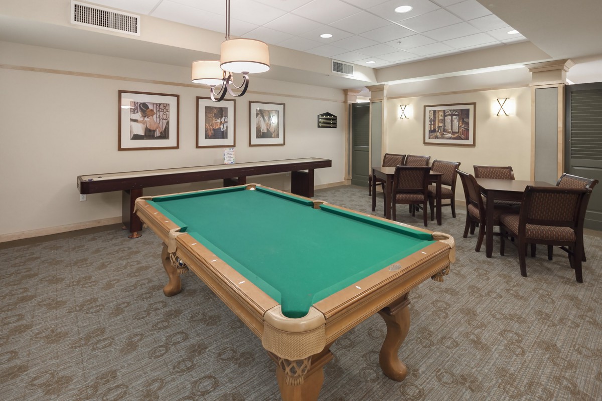 A recreation room featuring a pool table and seating area with framed artwork and overhead lighting.