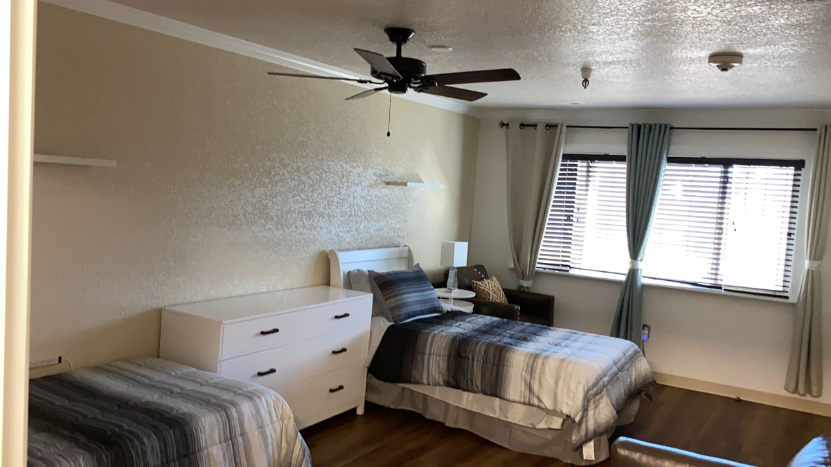 A cozy bedroom featuring two single beds, a dresser, and a window with curtains.