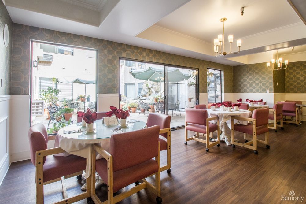 A well-lit dining room with tables and chairs, decorated with plants and floral arrangements.
