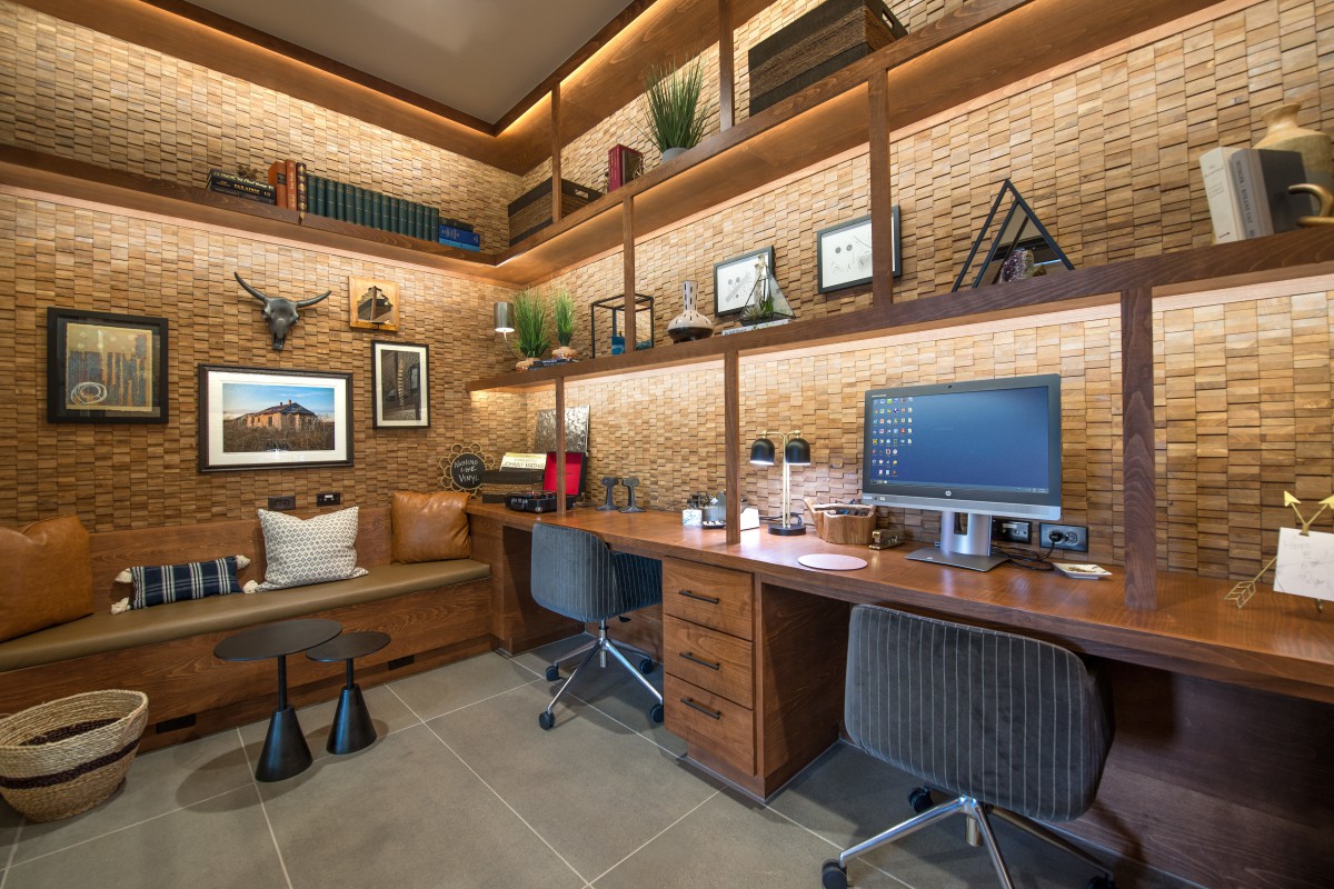 A modern office workspace featuring a wooden desk, computer setup, and decorative shelves on a brick wall.