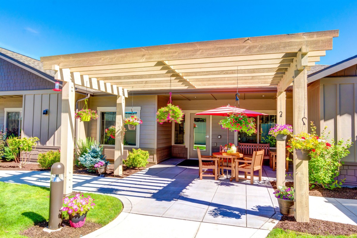 A sunny patio area with a wooden pergola, outdoor furniture, and hanging plants.