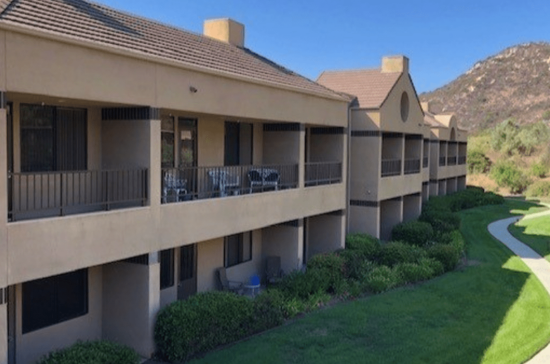 A row of residential apartments with balconies overlooking a lush green area.