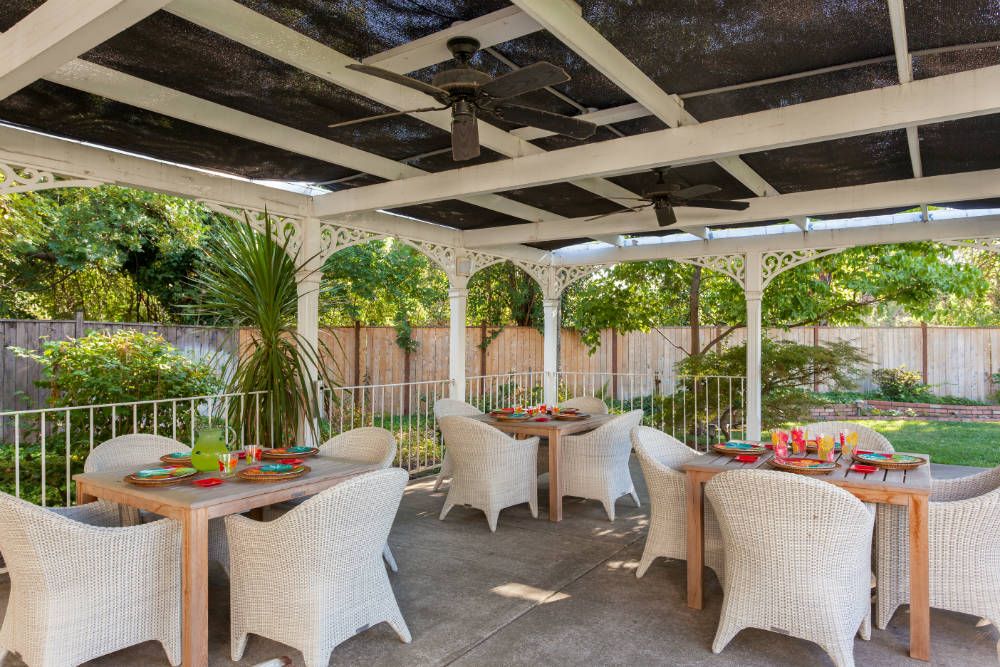 A beautifully set outdoor patio with wicker chairs and tables surrounded by lush greenery.